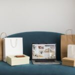 A laptop surrounded by shopping bags and boxes on a blue sofa, ideal for online shopping themes.